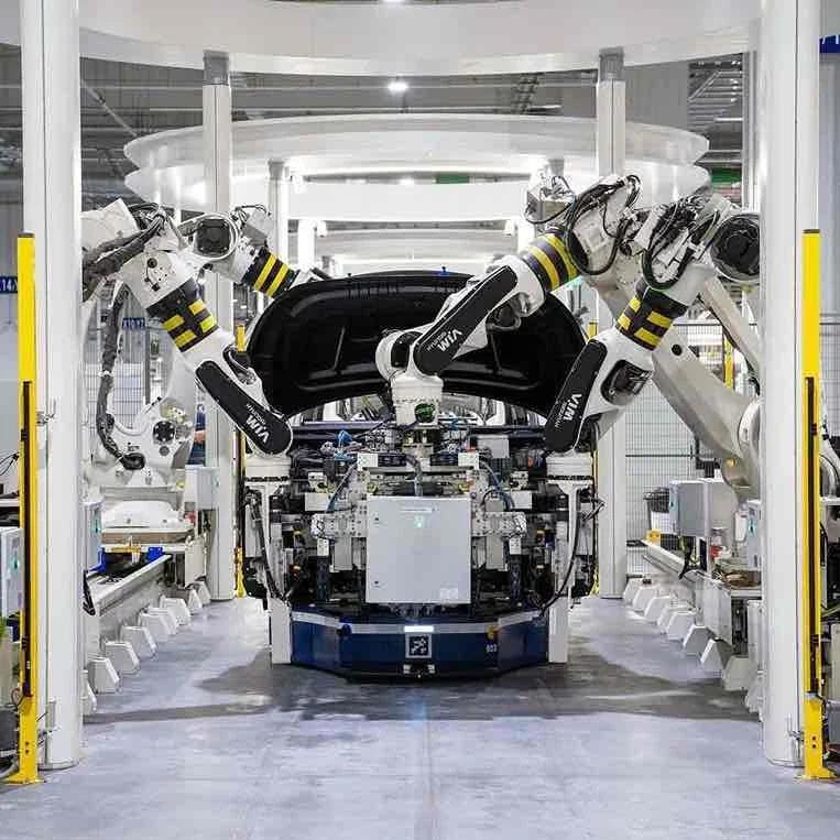 White robot arms assembling a car frame on a clean factory floor